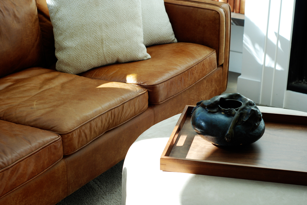 An organically shaped vase in contrast to the simpler shapes of the wood tray and circular ottoman.